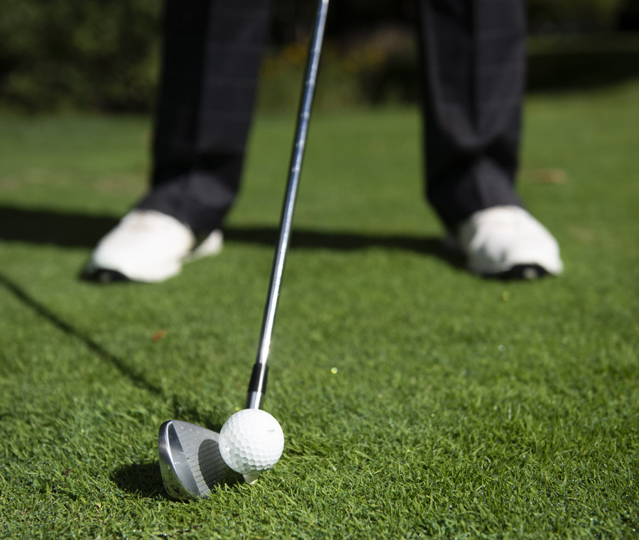 A golfer lining up their iron beside the golf ball to swing